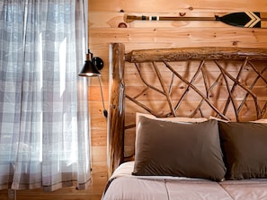 Una habitación tipo cabaña de madera con una cama, una lámpara y una tabla de remo apoyada en la pared.