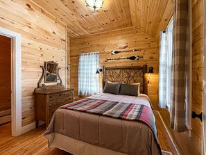 Acogedor dormitorio de cabaña de madera con cama, cómoda y espejo.