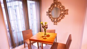 Una zona de menjador amb una taula de fusta, quatre cadires, un vas amb flors i un mirall decoratiu a la paret.