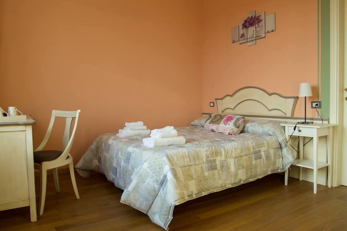 Quarto com cama, cadeira, escrivaninha e mesa de cabeceira.