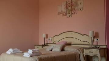Un letto rifatto con cura, con copriletto e cuscini color beige, due comodini con lampade e un muro decorato con tre quadri floreali.