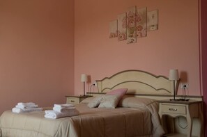 A neatly made bed with a beige bedspread and pillows, two bedside tables with lamps, and a wall with three framed floral paintings. - Locanda Corte Roveri (Bologna)