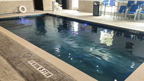Una piscina con un cartel de prohibido bucear, un neumático y un bote de basura.