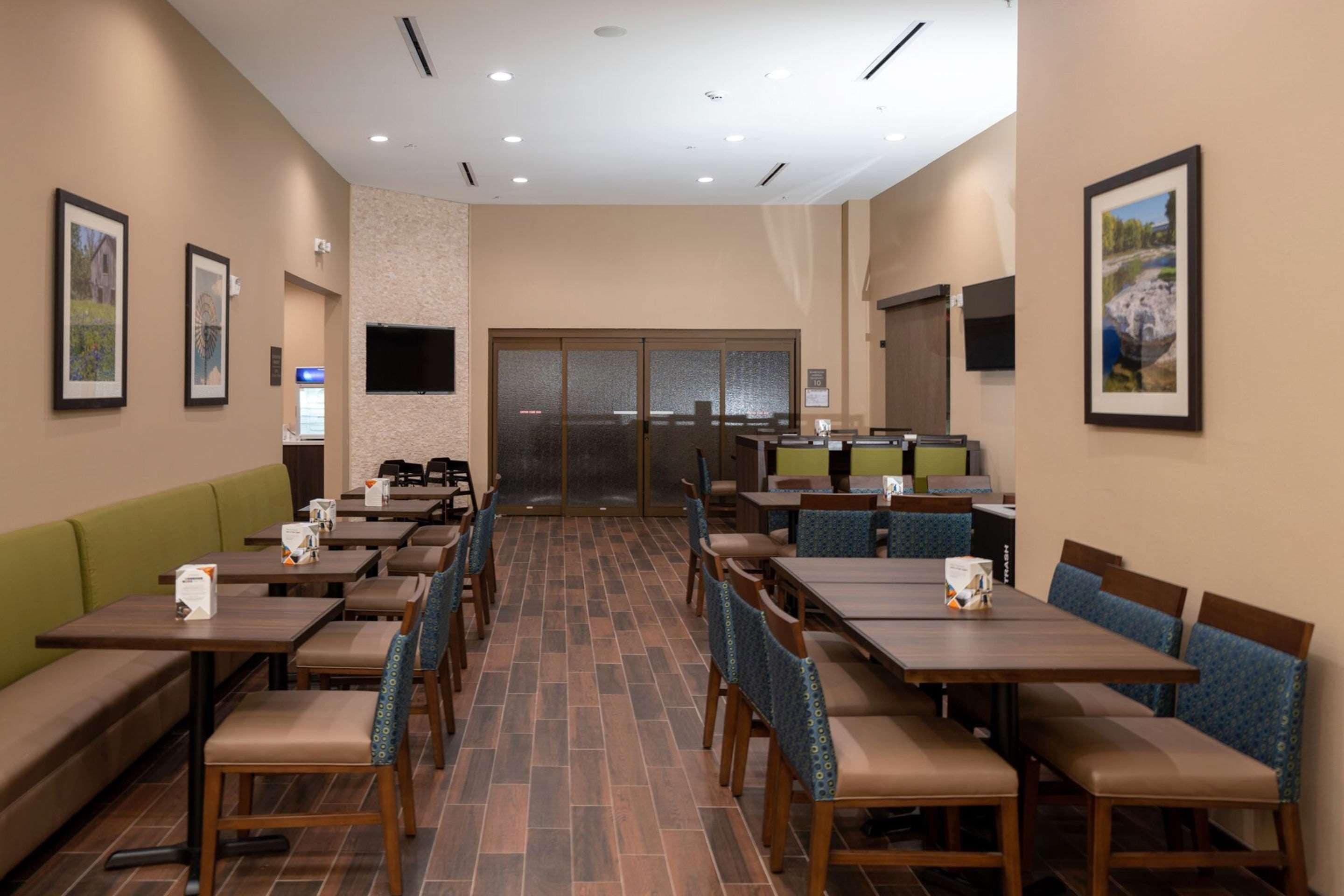 Comedor de hotel con varias mesas y cabinas, un sofá verde y cuadros en las paredes.