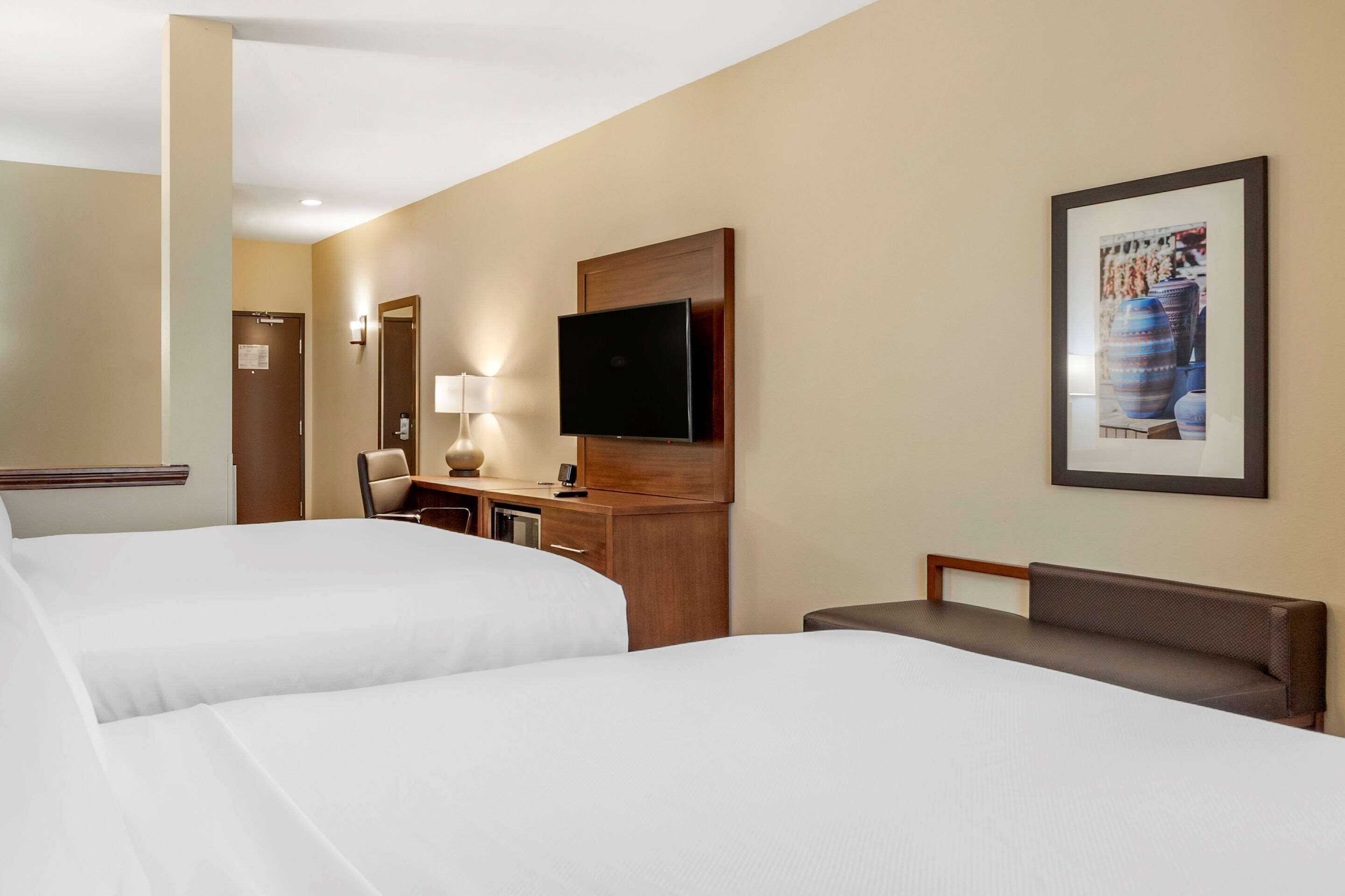 Habitación de hotel con dos camas, un escritorio con lámpara, un televisor y un cuadro en la pared.