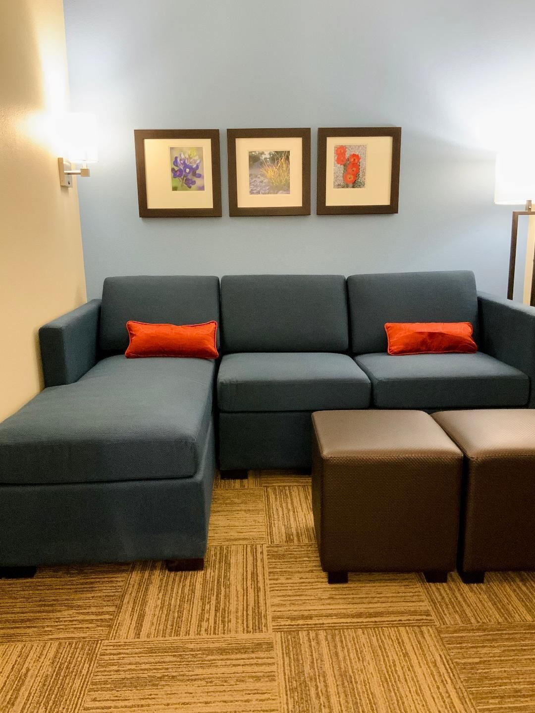 A modern living room with a sectional sofa, a brown ottoman, and three framed pictures on the wall.