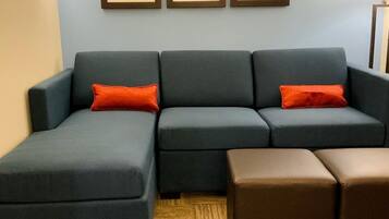 A modern living room with a sectional sofa, a brown ottoman, and three framed pictures on the wall.
