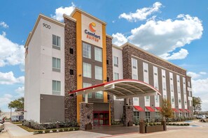 Un hotel Comfort Suites con diseño moderno, que presenta una entrada destacada con toldo rojo y fachada de piedra.