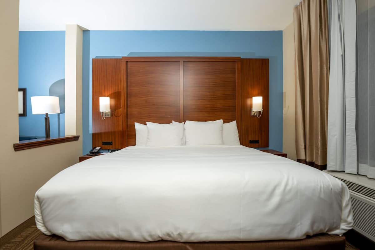 Habitación de hotel con una cama grande, cabecero de madera, dos lámparas de noche y una ventana con cortinas.