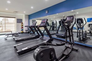 Un gimnasio con cintas de correr, elípticas y un muro de espejos.
