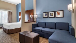 Habitación de hotel con cama, sofá, un pequeño otoman y cuadros en la pared.