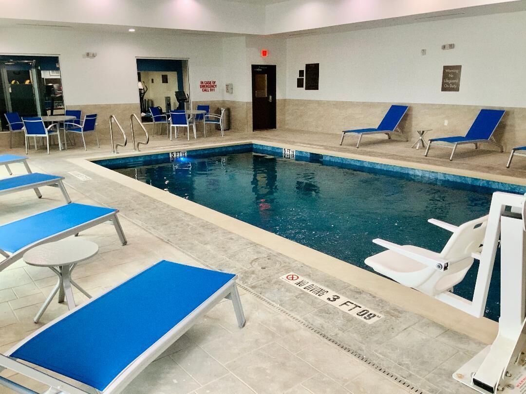 Piscina interior com espreguiçadeiras azuis e brancas, um posto de salva-vidas e uma placa indicando profundidade de 0,9 metros.