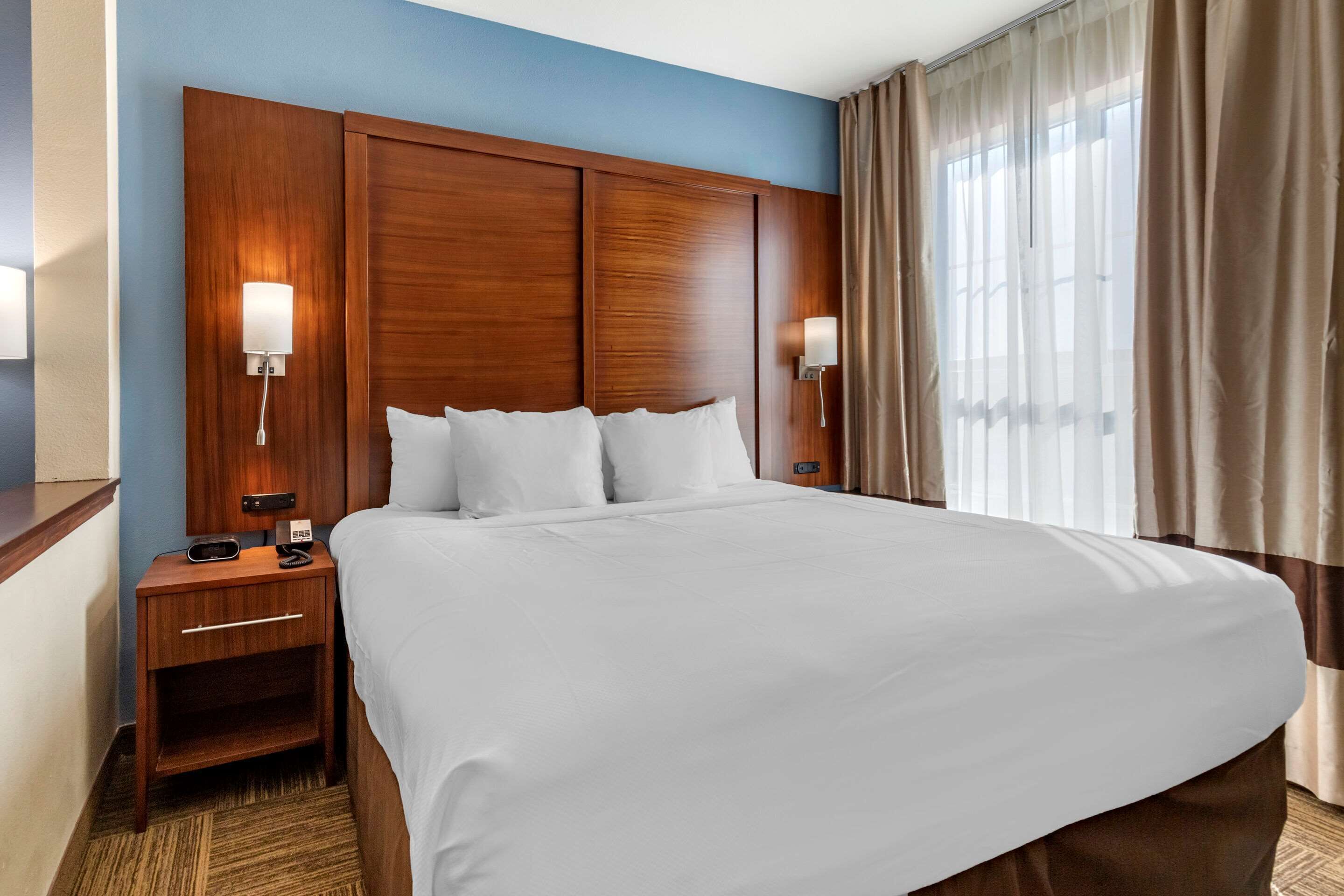 A hotel room with a large bed, wooden headboard, two bedside tables with lamps, and a window with curtains.