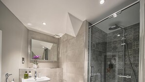 Un baño moderno con ducha de vidrio, lavamanos blanco y retrete.