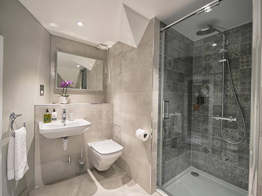 Et moderne badeværelse med en glasafskærmet brusekabine, en hvid vask og et toilet.