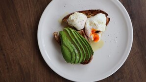 Un plato blanco con una rebanada de tostada cubierta de aguacate y un huevo escalfado.
