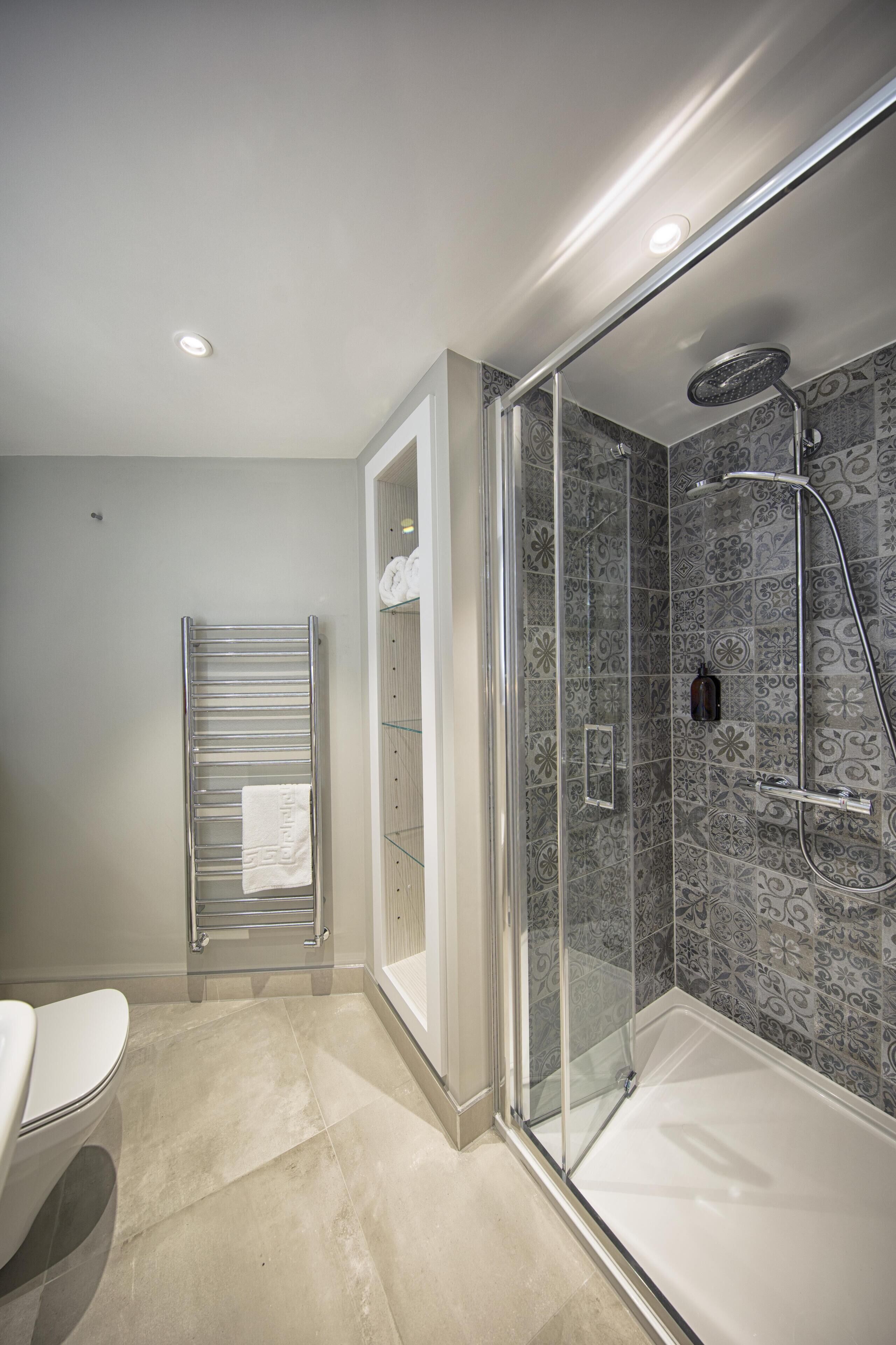 A modern bathroom with a glass-enclosed shower, a toilet, and a towel rack.
