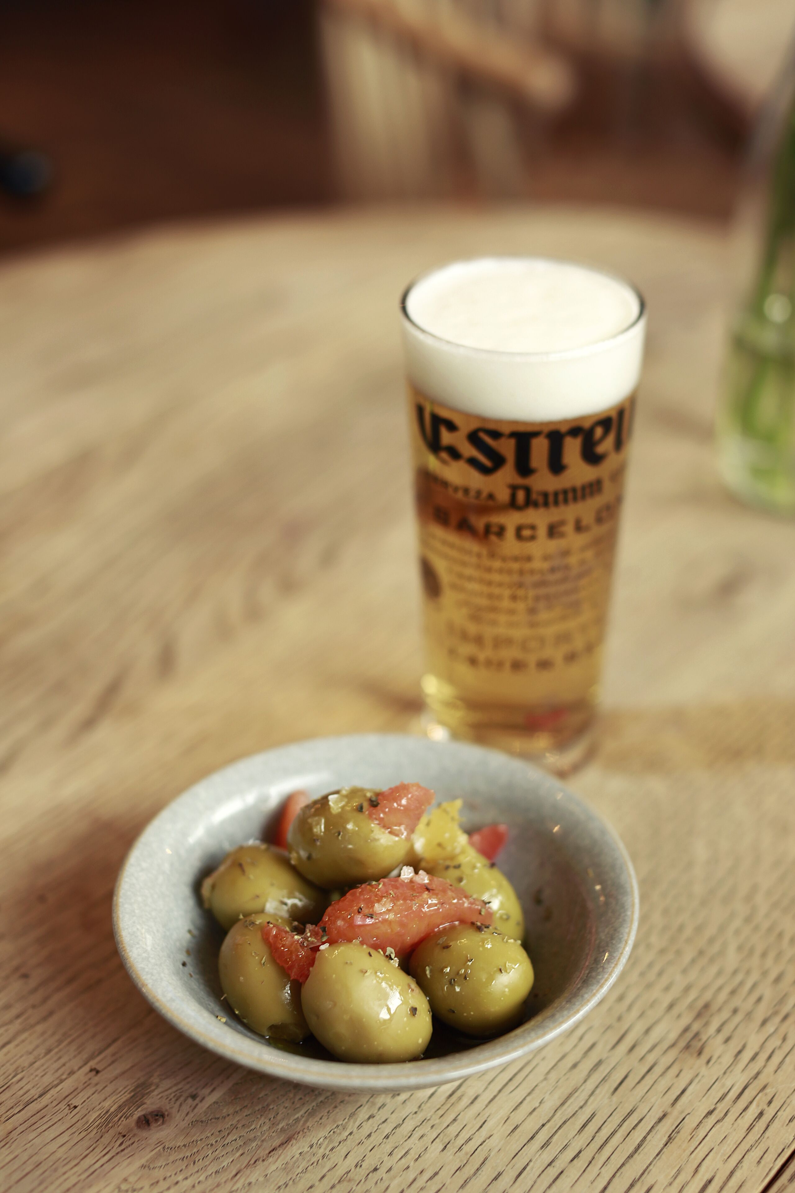 A small bowl of olives and a glass of beer on a wooden table.