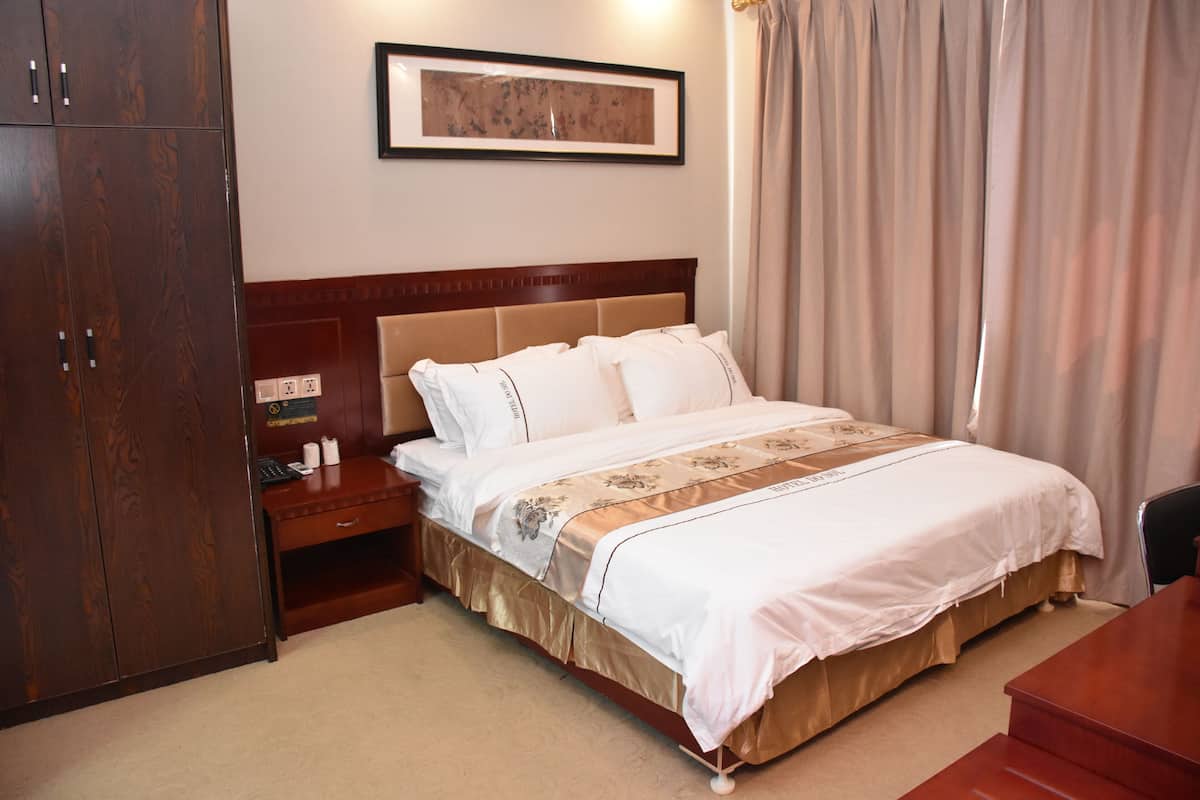 Habitación de hotel con una cama grande, armario de madera, mesita de noche y un cuadro enmarcado en la pared.