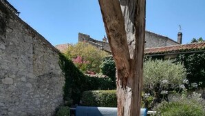 Un área junto a la piscina con un muro de piedra, un tronco de árbol de madera y mobiliario exterior, incluyendo una silla de mimbre y una pequeña mesa.