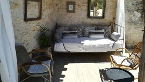 Una habitación acogedora con cama, sillas de mimbre, una lámpara colgante y una pared de piedra.