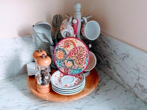 A kitchen counter with a marble surface, a wooden tray holding a pepper grinder, a salt shaker, and a stack of plates with a colorful design. - Wexford Townhouse (Wexford)