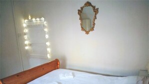 A neatly made bed with white linens, a wooden headboard, a mirror with a decorative frame, and a string of lights on the wall. - Wexford Townhouse (Wexford)