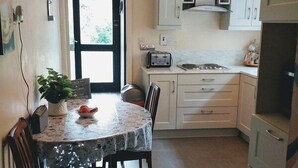 A compact kitchen with white cabinets, a dining table with chairs, a toaster, and a hanging light fixture. - Wexford Townhouse (Wexford)