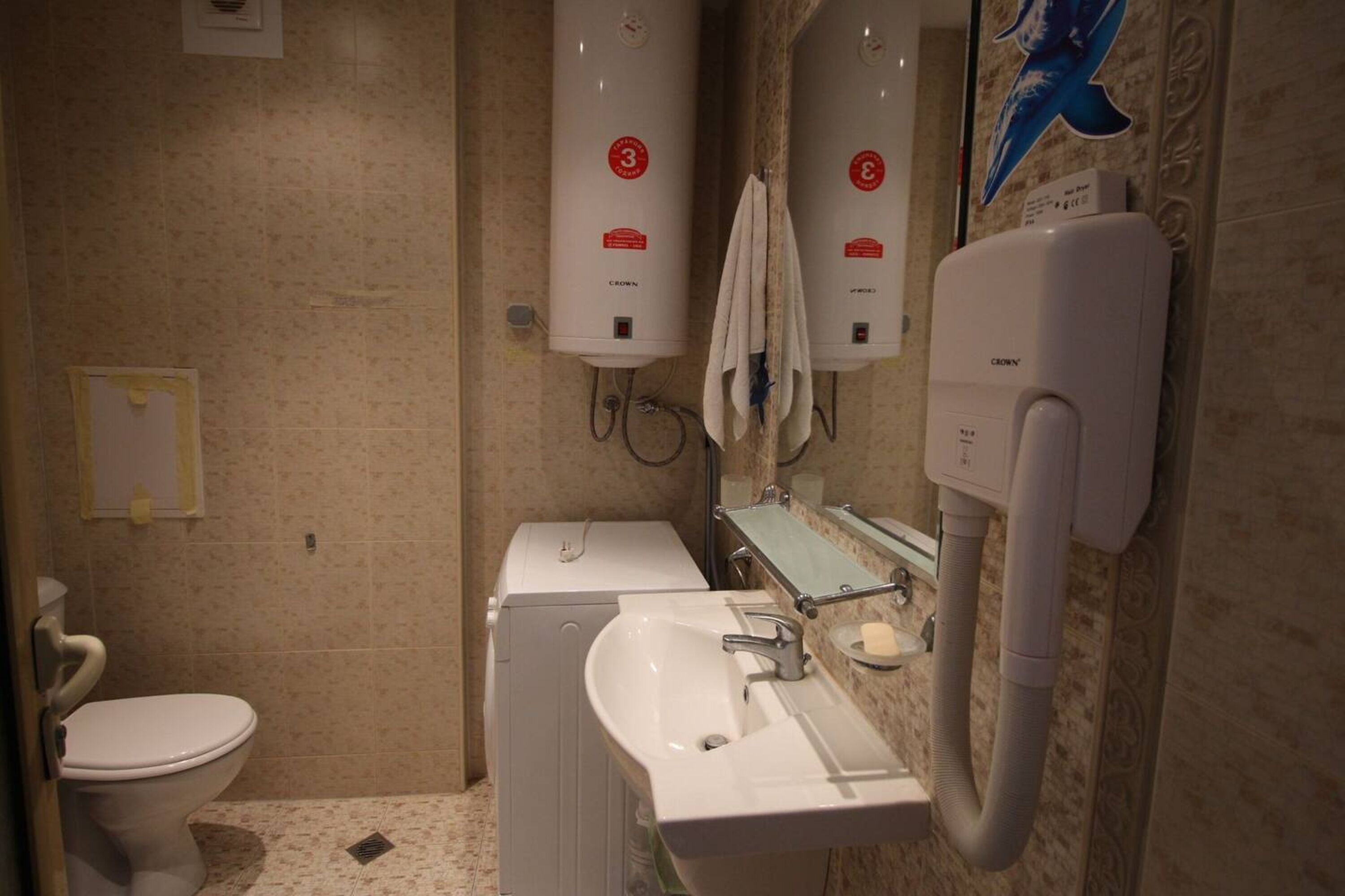 A bathroom with a toilet, a sink, a mirror, and two water heaters labeled 'CROWN'.