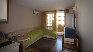 Habitación compacta con cama, una mesita, una silla, kitchenette y ventana con cortinas.