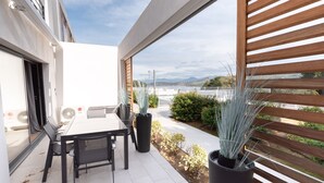 A modern outdoor patio with a table and chairs, potted plants, and a view of a body of water and mountains. - L'Ebène - Bel appt pour 6 personnes avec vue mer (Coti-Chiavari)