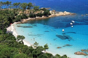 A coastal beach with clear turquoise waters, rocky outcrops, and a sandy shoreline.