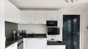 A modern kitchen with white cabinets, a black countertop, a built-in oven, and a black door. - L'Ebène - Bel appt pour 6 personnes avec vue mer (Coti-Chiavari)