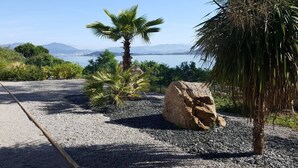 A gravel pathway with palm trees and a large rock, leading to a scenic overlook with a view of the sea and distant mountains. - L'Ebène - Bel appt pour 6 personnes avec vue mer (Coti-Chiavari)
