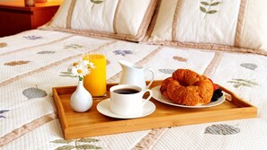 A breakfast tray with a croissant, coffee, a glass of orange juice, and a small vase with flowers on a bed with a floral-patterned bedspread. - Villa Patrizia Siena (Siena)