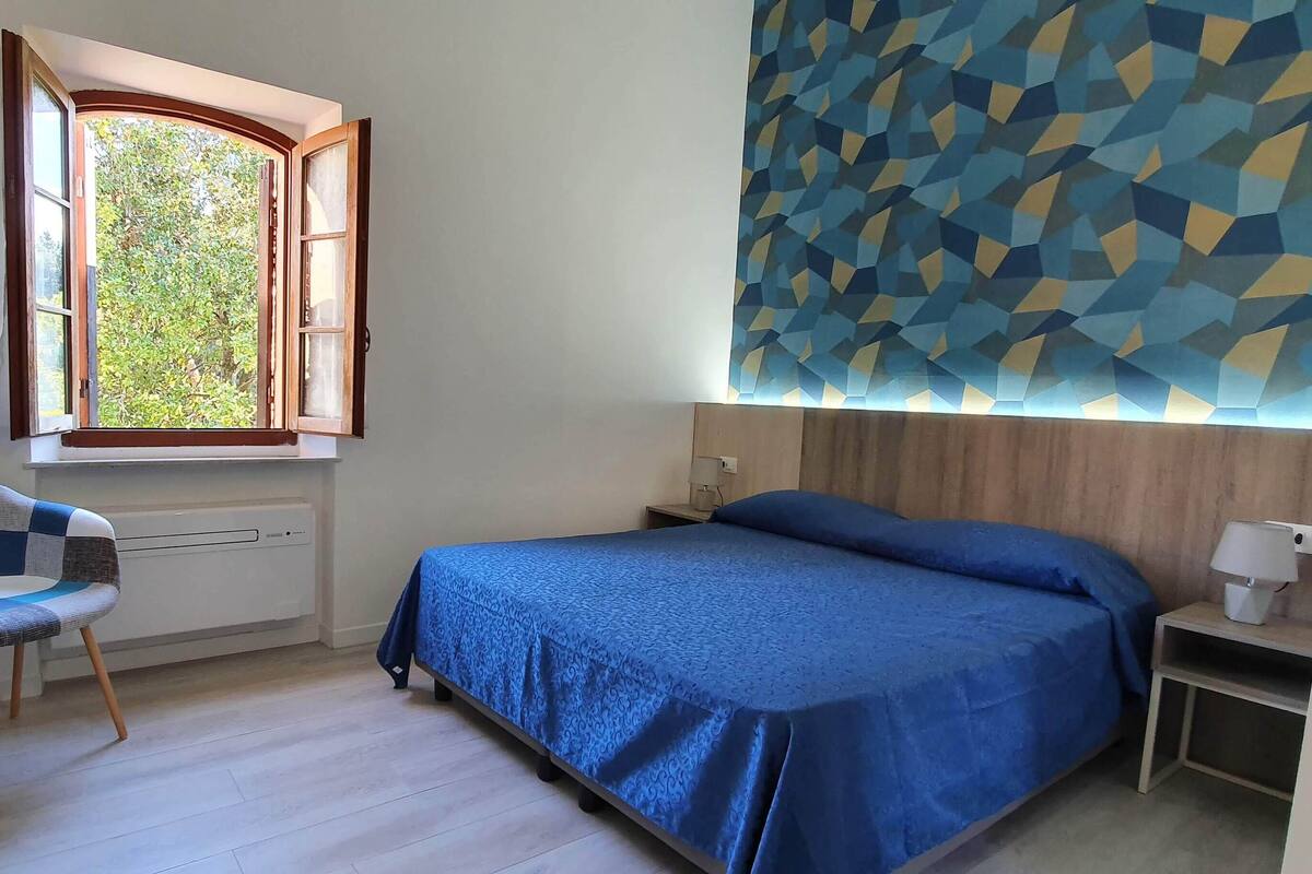 A bedroom with a bed, a desk, a chair, a window, and a geometric-patterned wall.