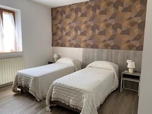 A hotel room with two single beds, a geometric-patterned wall, a window with curtains, and a bedside table with a lamp. - Villa Patrizia Siena (Siena)