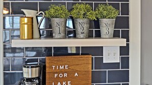 Une cuisine équipée d’une machine à café, d’une pancarte sur laquelle on peut lire « Il est temps de faire une pause au bord du lac », et de trois plantes en pot, chacune portant une étiquette.