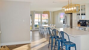 Une cuisine moderne dotée d’un grand îlot central, de meubles blancs et de tabourets de bar bleus.