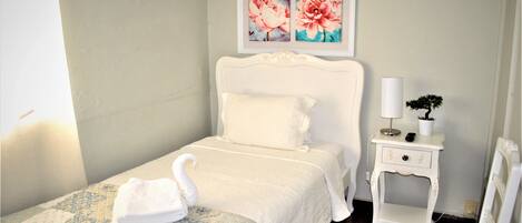A neatly made bed with a swan-shaped pillow, a bedside table with a lamp, and a framed floral artwork above the bed.