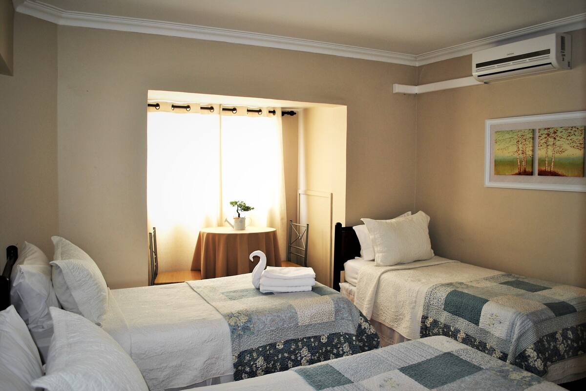 A hotel room with two beds, a small table with a plant, and a painting on the wall.