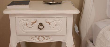 A white bedside table with a lamp, a book, and a small decorative item.