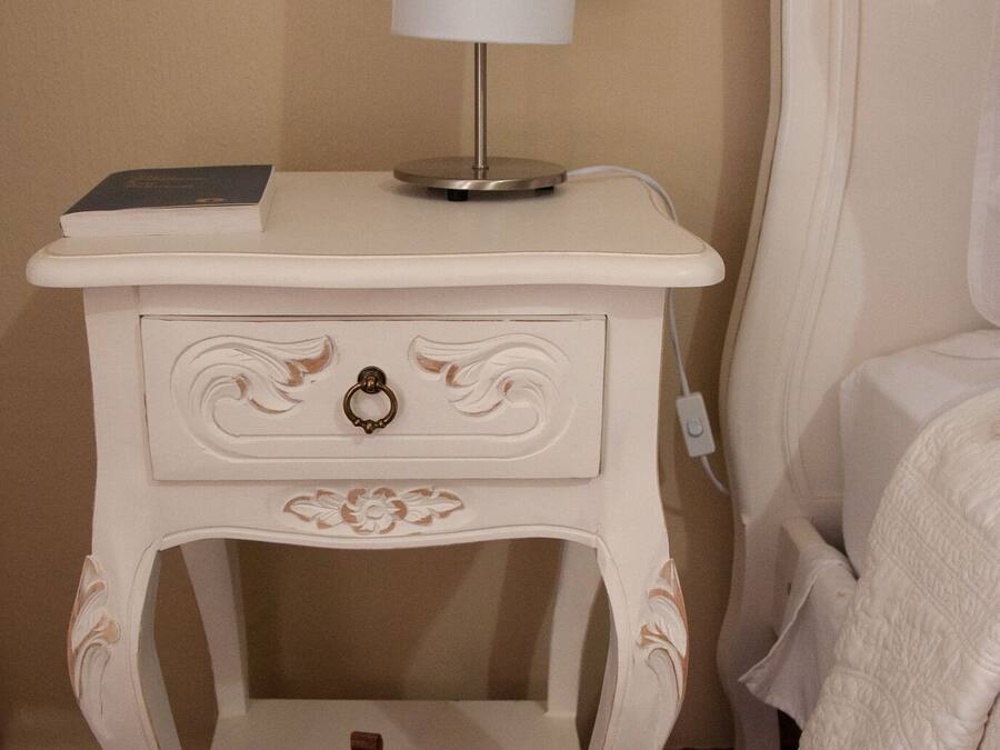 A white bedside table with a lamp, a book, and a small decorative item.