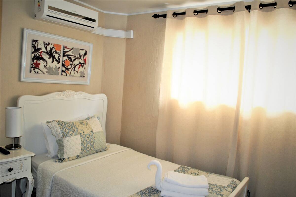 A neatly made bed with a quilt, a bedside lamp, and a framed artwork on the wall.
