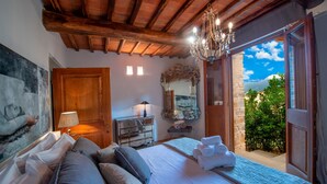 Ein Schlafzimmer mit einem großen Bett, einer Lüster, einem Spiegel und Blick auf Grünflächen.