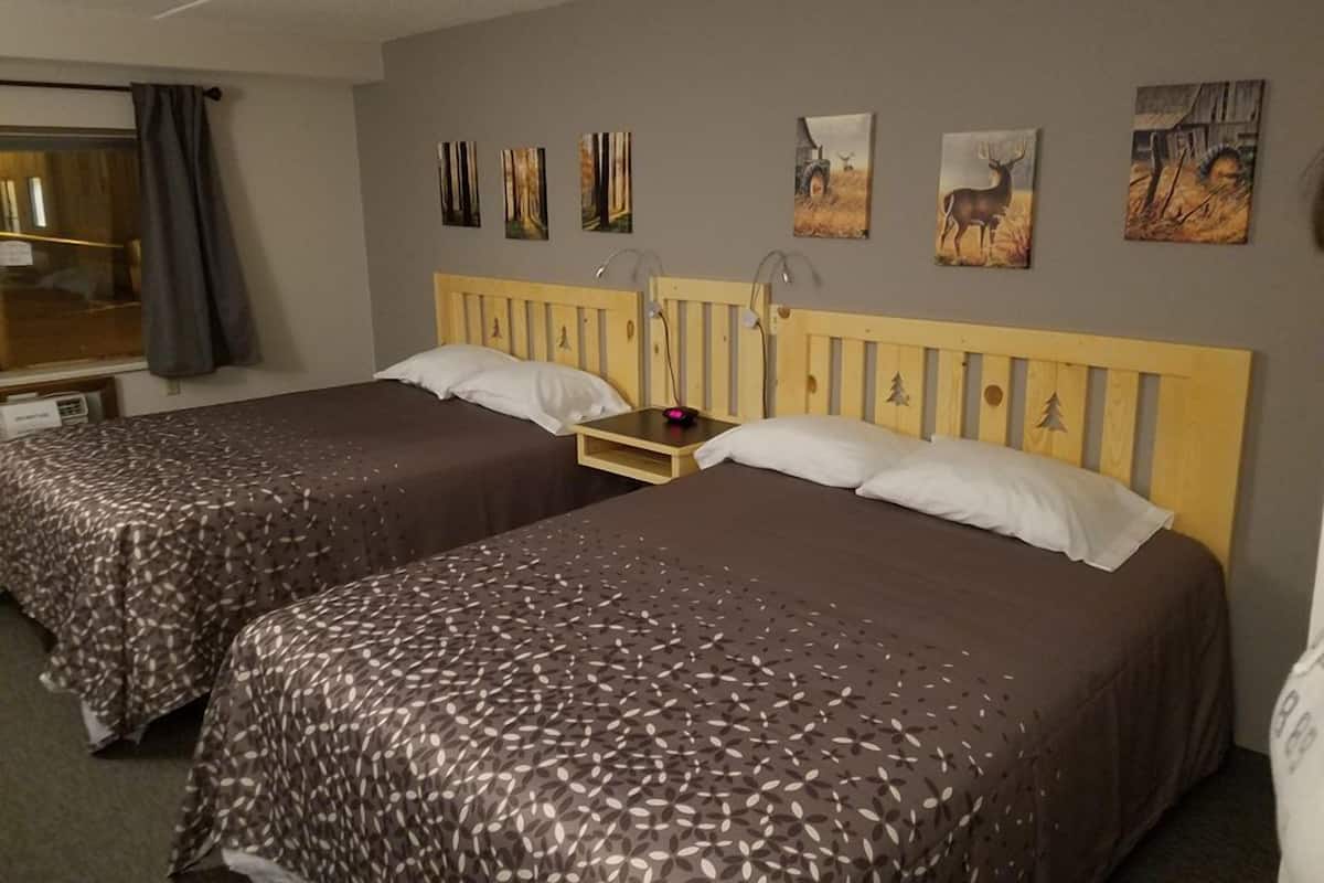 A hotel room with two beds, a wooden headboard, a bedside table with a lamp, and artwork on the wall.