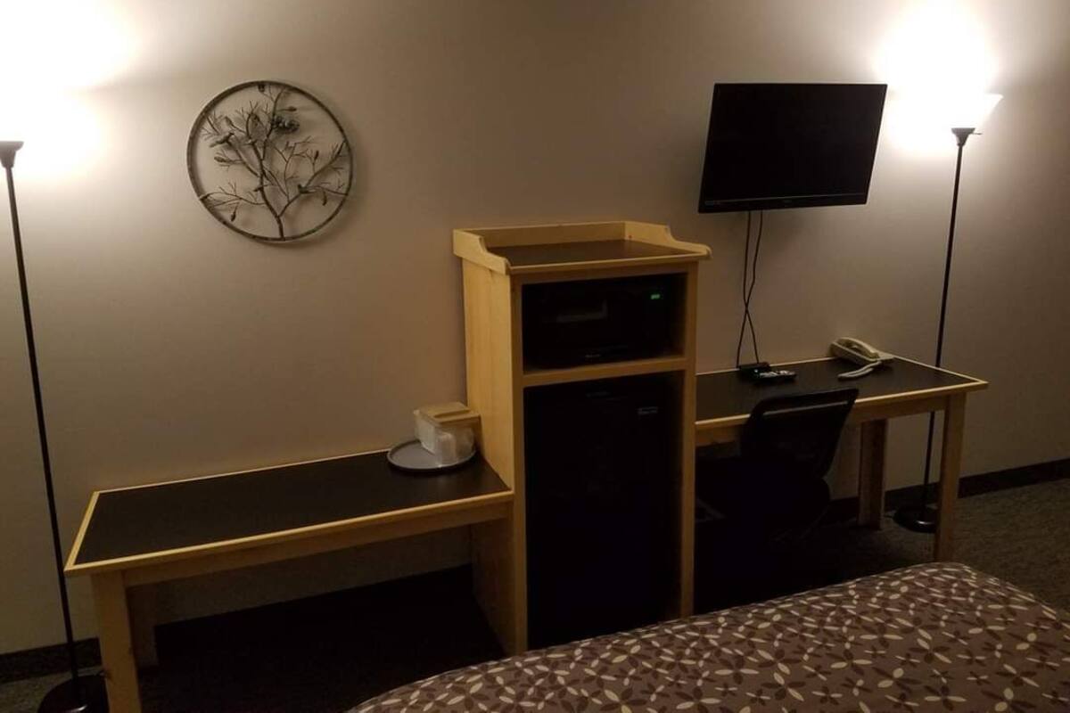 A hotel room with a bed, a desk with a computer, a TV, and a wall-mounted artwork.