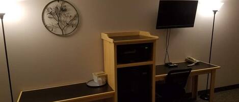 Una habitación de hotel con una cama, un escritorio con computadora, un televisor y una obra de arte en la pared.