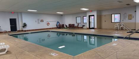 An indoor swimming pool with a tiled floor, chairs, a lifebuoy, and a door.