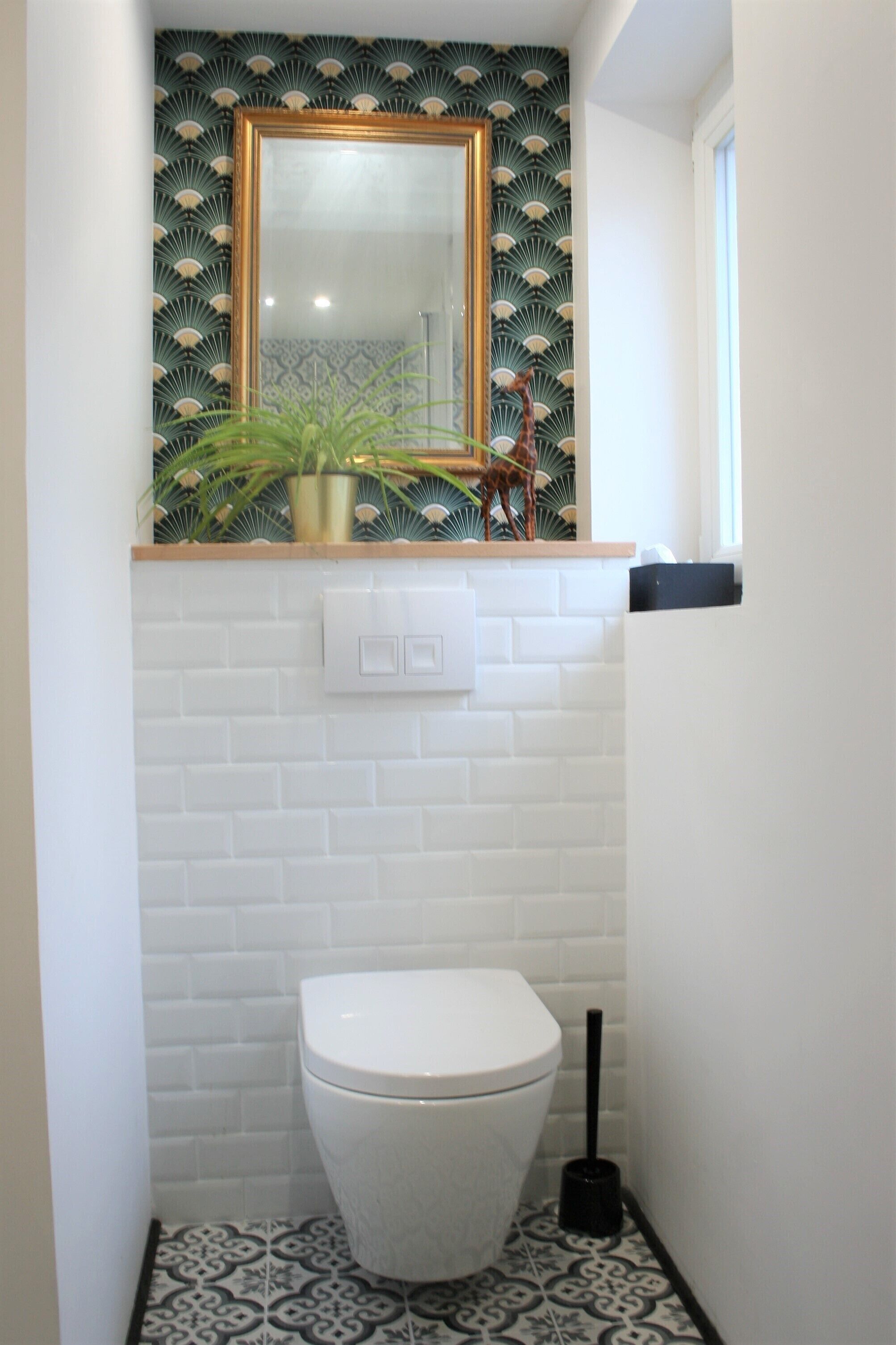 Een badkamer met een wit toilet, een spiegel met gouden lijst en een behang met patroon.